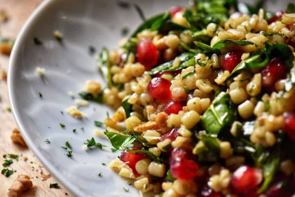 A simple fregola spinach pomegranate salad is plated in a large white bowl.