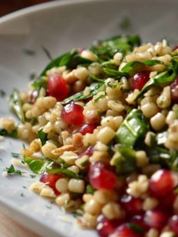 A colorful bowl of the Simple Fregola Spinach Pomegranate Winter Salad is shown.