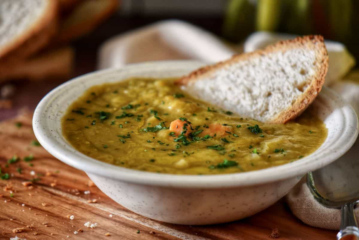 A slice of whole wheat bread with a bowl of pea soup.