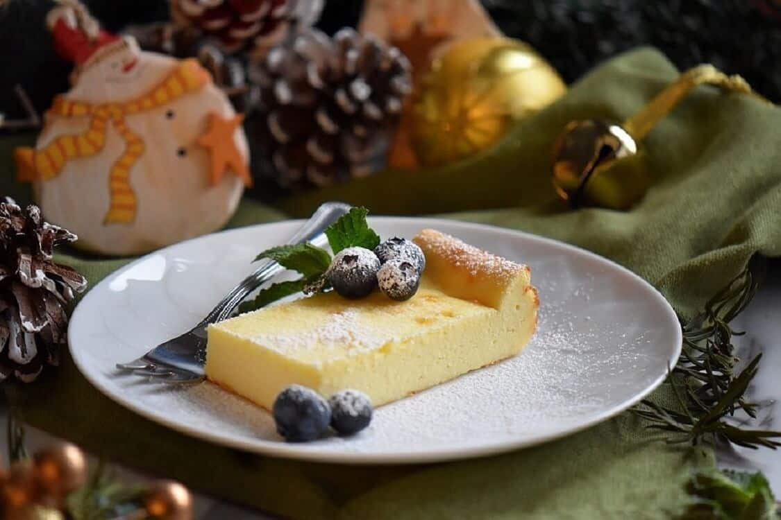 A plate of ricotta cake served with a few blueberries and sprinkled with icing sugar.