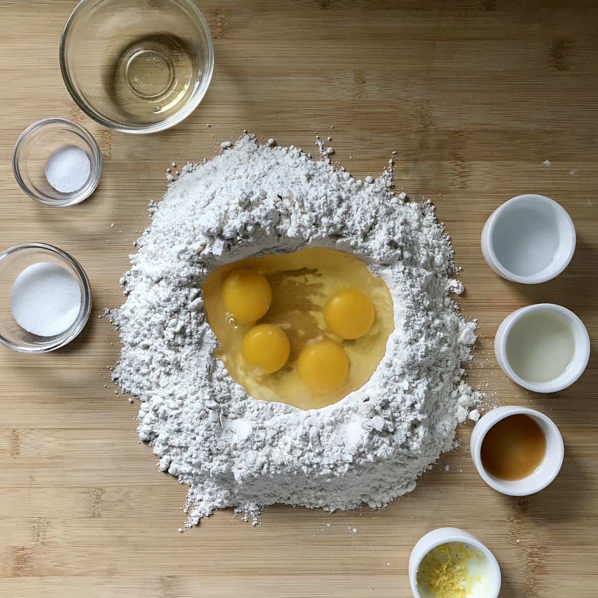 Eggs inside a flour well, surrounded by the rest of the ingredients to make a struffoli recipe.