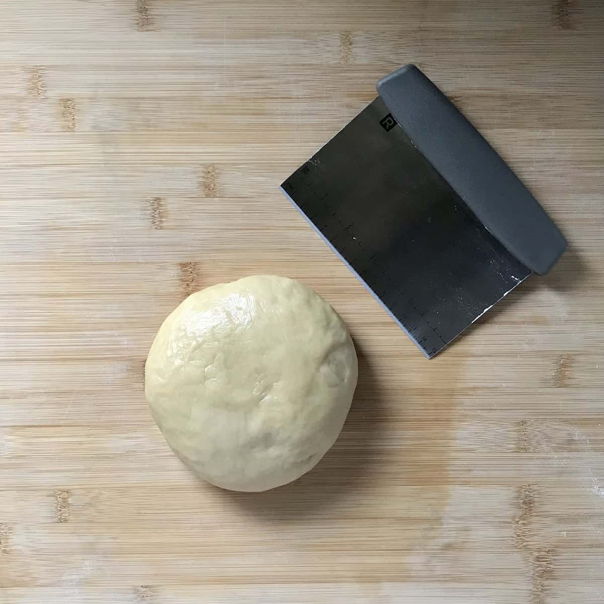 A ball of struffoli dough next to a dough scraper.