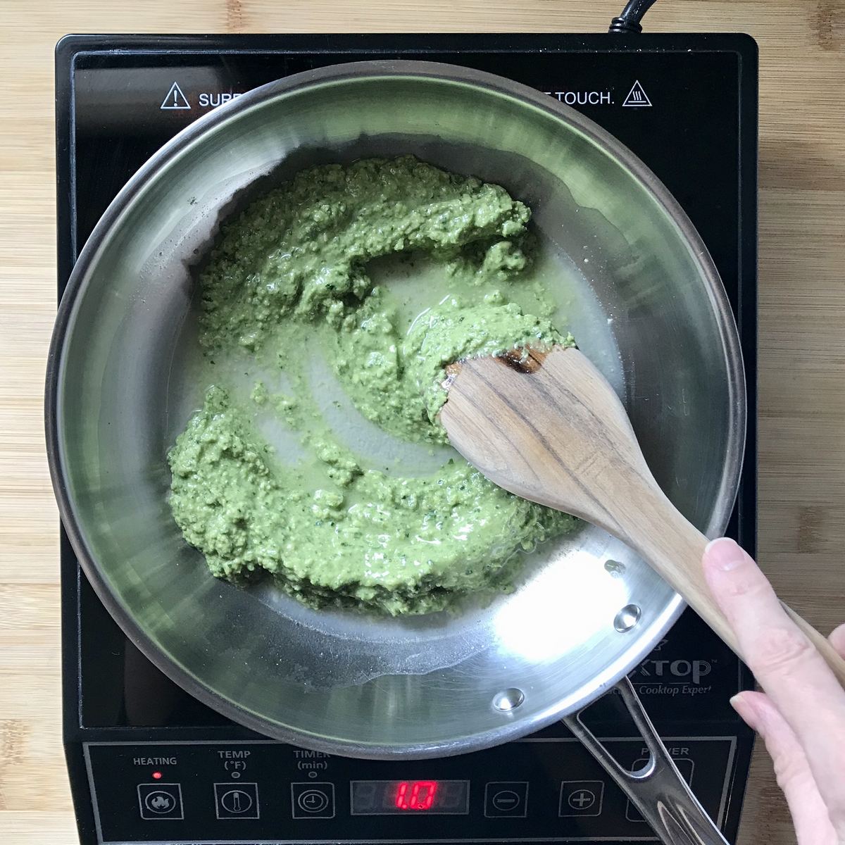 Pasta water is added to the pesto sauce in a pan. 