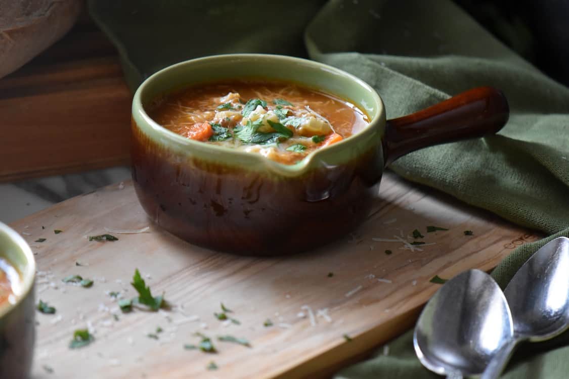 A small bowl of lentil pasta soup on a wooden board.