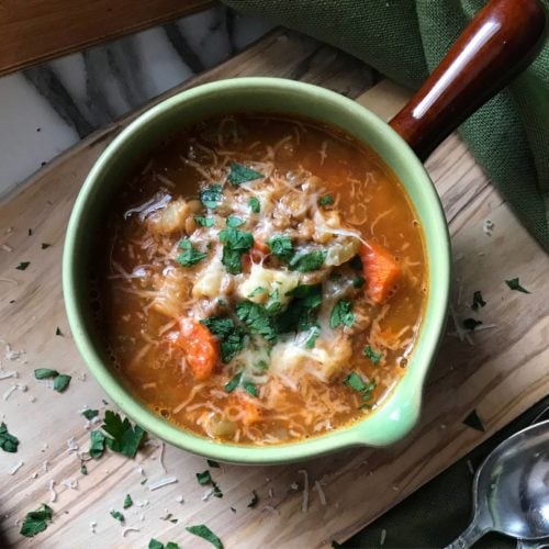 A bowl of pasta and lentils garnished with grated cheese and parsley.