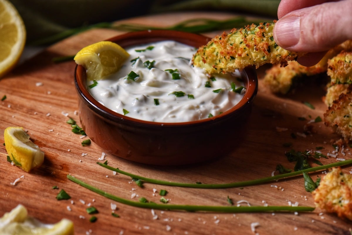 Air fryer zucchini sticks being dipped in the yogurt sauce.