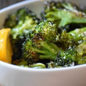 The crispy edges of oven roasted broccoli next to a lemon wedge.