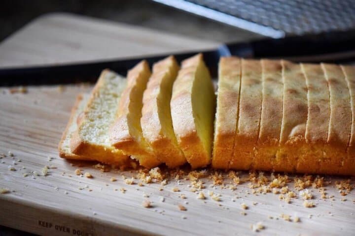 A sliced loaf of anise biscotti on a wooden board surrounded by crumbs.