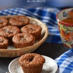 A bran muffin on a plate. In the background, a basket of muffins.