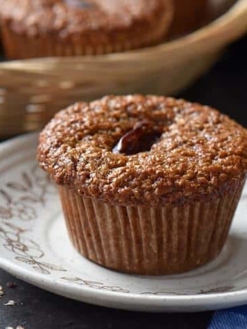 A close up of a bran muffin on a plate with some natural bran sprinkled on the table top.