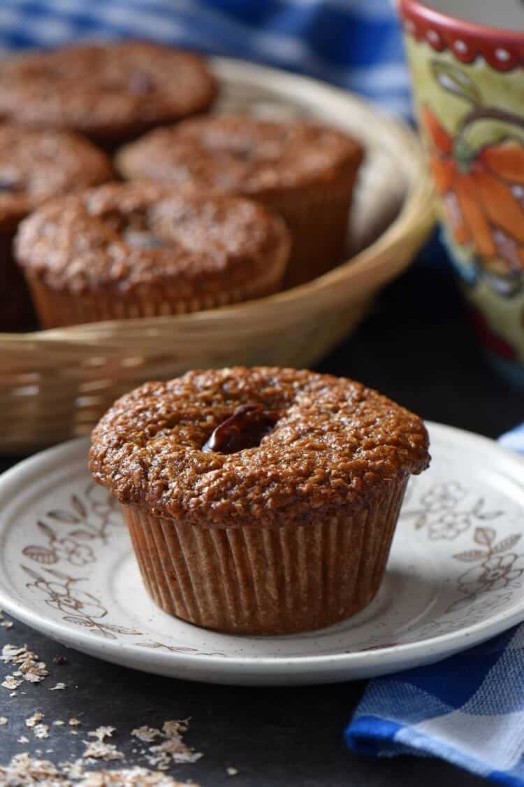 A close up of a bran muffin on a plate; a basket of muffins can be seen in the background.
