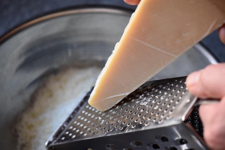 A box grater is used to grate Parmesan cheese for the crescia recipe.