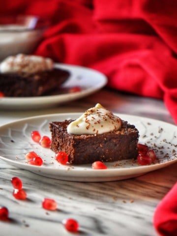 A close up shot of a square piece of Healthy Chocolate Brownie topped with whipped ricotta and surrounded with pomegranate arils.