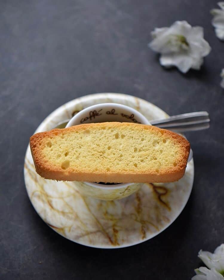 An overhead close up shot of a single Italian anise biscotti on an espresso cup.