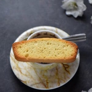 A close up of a single Italian anise biscotti on an espresso cup.