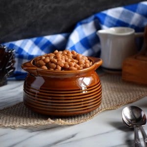 A side view of a brown ceramic dish of baked beans.