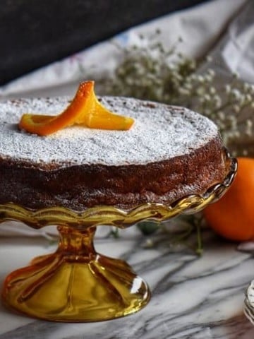 Rice ricotta Easter pie in a cake stand surrounded by oranges and lemons in the background.