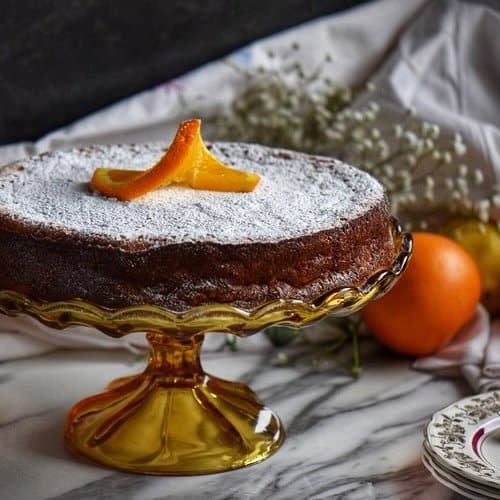 Rice ricotta Easter pie in a cake stand surrounded by oranges and lemons in the background.