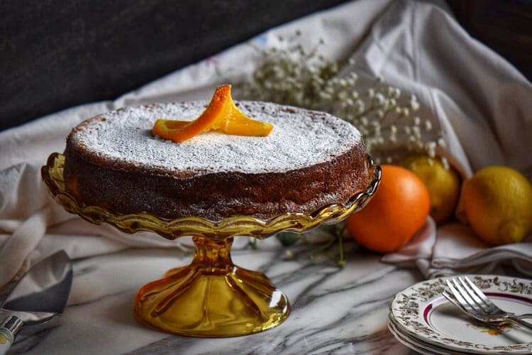 Rice ricotta Easter pie on a cake stand surrounded by oranges and lemons in the background.