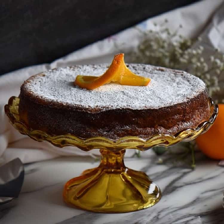 The rice ricotta Easter pie set on a cake platter with a dusting of icing sugar and a slice of orange placed decoratively over the top.