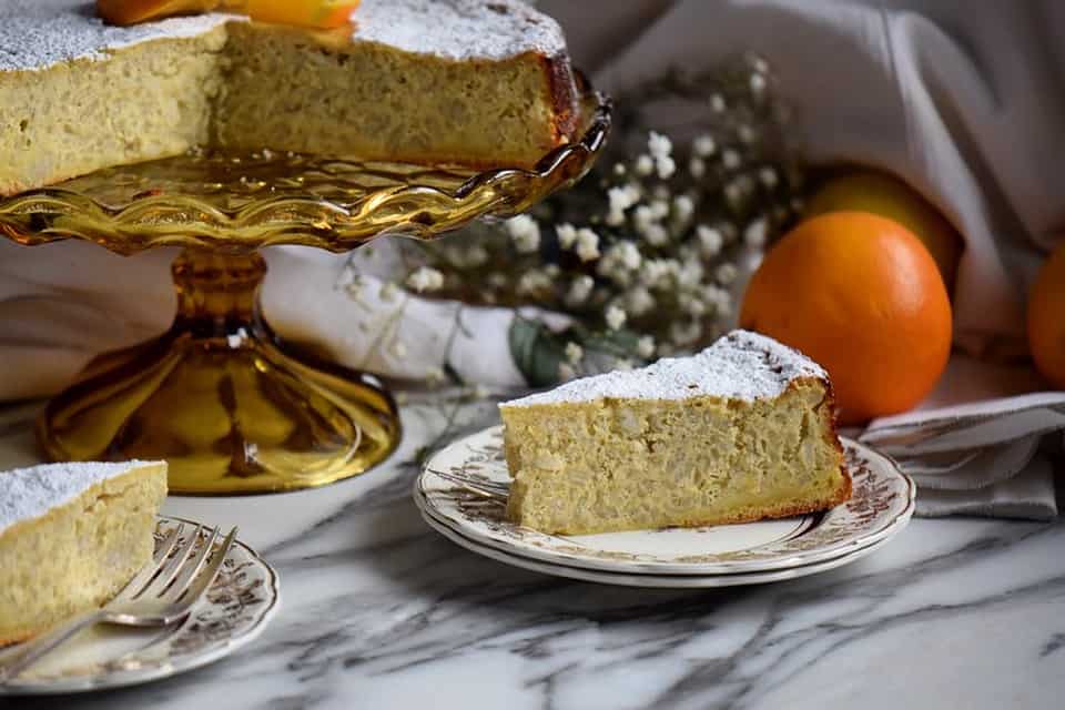 A slice of rice ricotta Easter pie in a plate placed next to the pie on the cake pedestal.