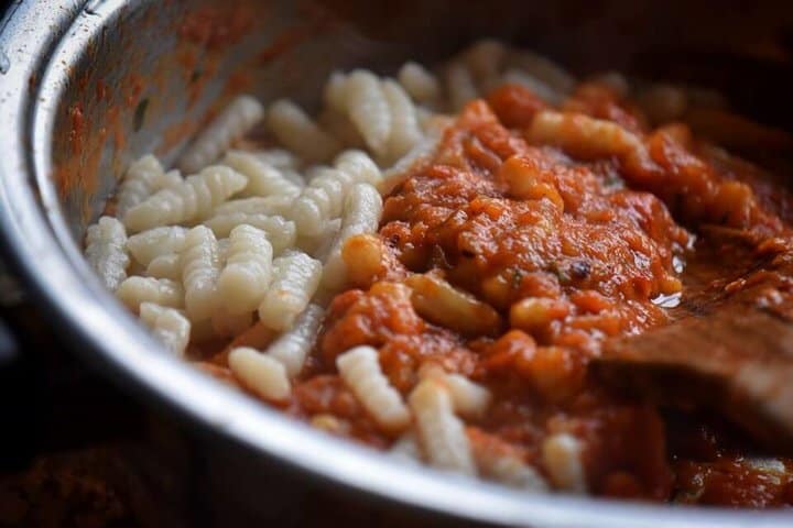 Roasted red pepper sauce and cavatelli being combined.