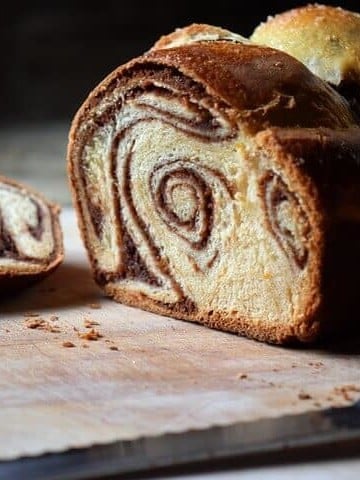 A freshly sliced loaf of cozonac is on a wooden board.