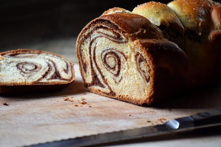 A freshly sliced loaf of cozonac is on a wooden board.