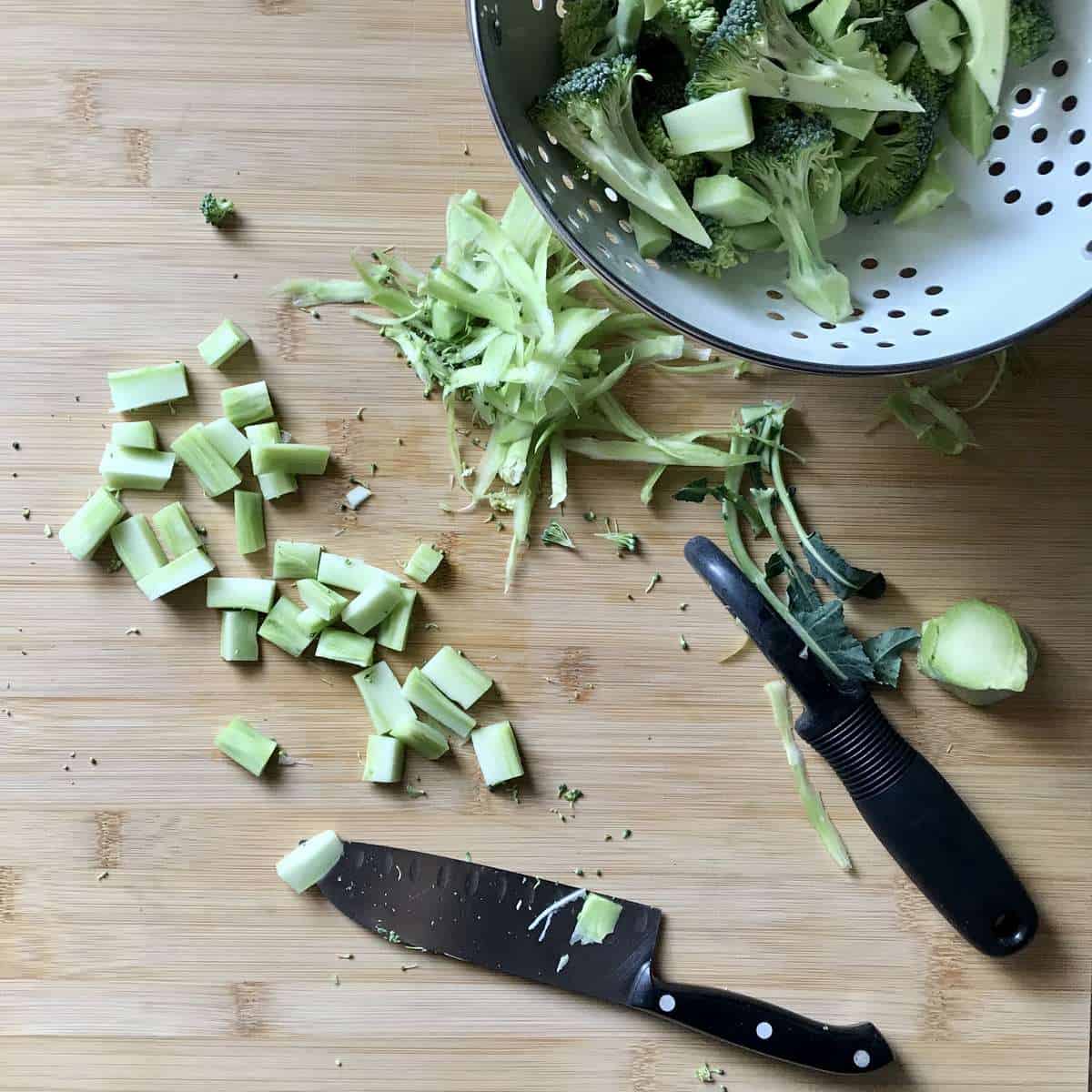 Chopped broccoli stalks on a wooden board, next to a knife.