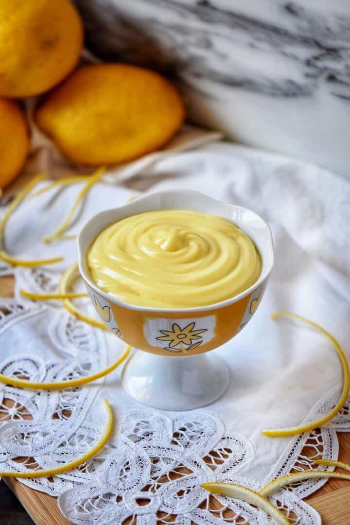 A bowl of pastry cream surrounded by lemon peels and lemons.