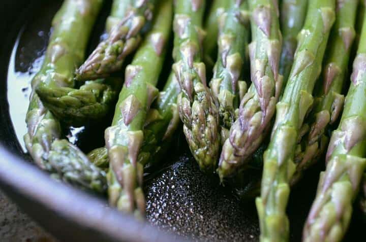 Asparagus tips shown in a cast iron pan being sautéed.