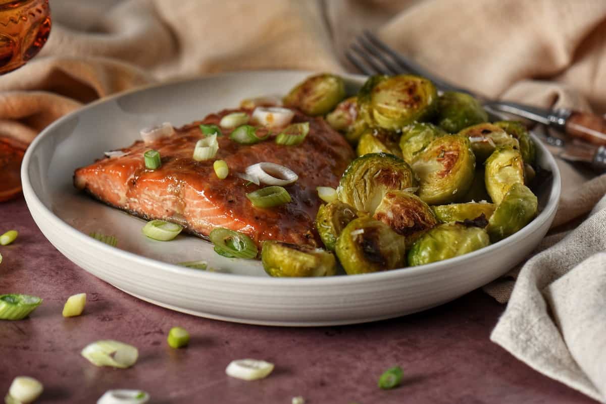 A close up picture of a maple glazed salmon served on a white plate.