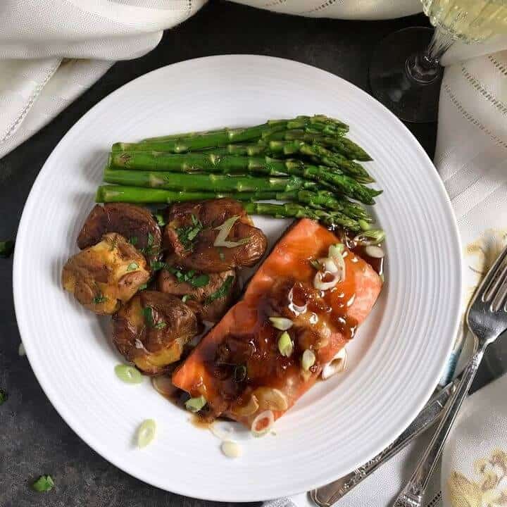 An overhead shot of a white dinner plate with glazed salmon, sauteed asparagus and smashed potatoes.