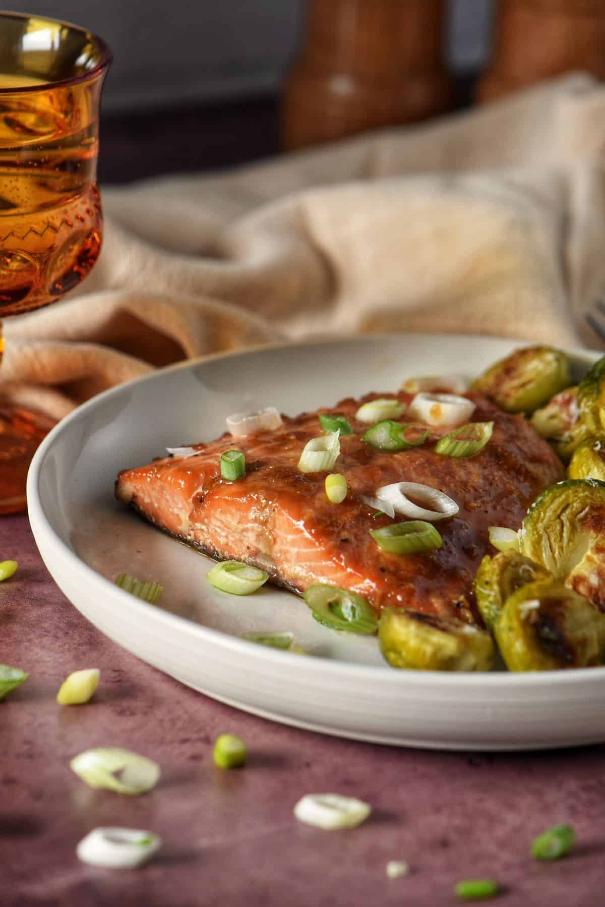 Baked salmon and garlic roasted brussels sprouts on a white dinner plate with a glass of white wine in the background.