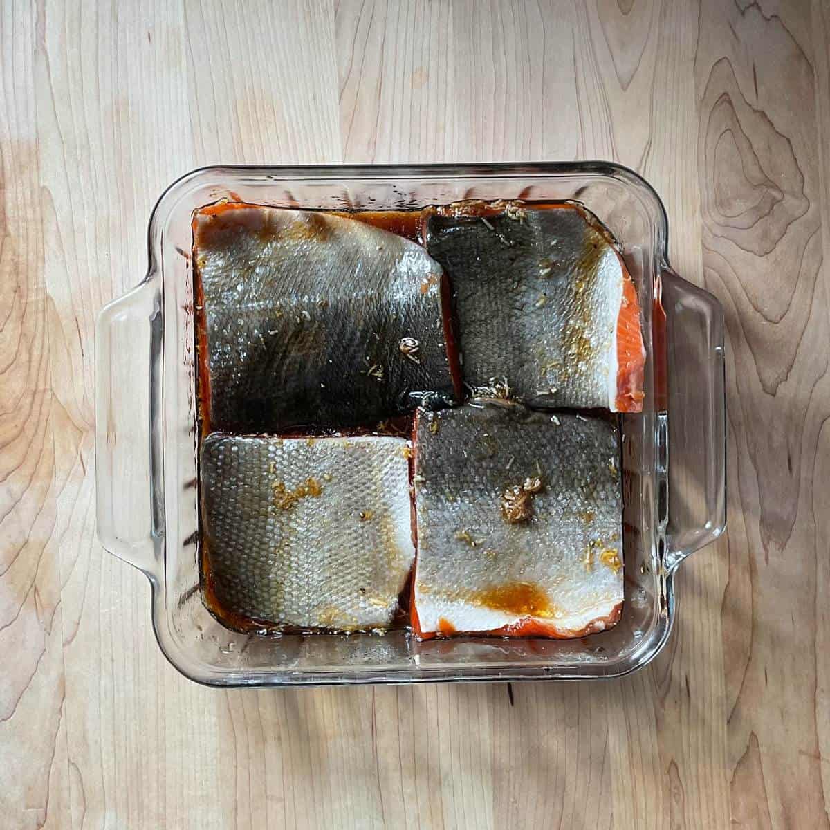 Salmon fillets marinating in a glass baking dish.