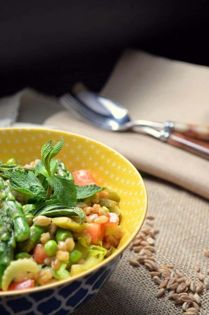 The colorful farro spring salad in a yellow bowl. A bowl of the pea farro salad along side a few scattered grains of farro.