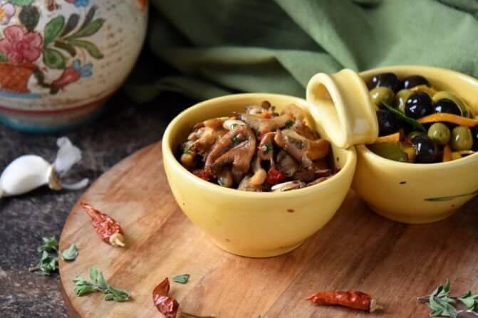 Marinated Mushrooms along side marinated olives, both in yellow bowls.