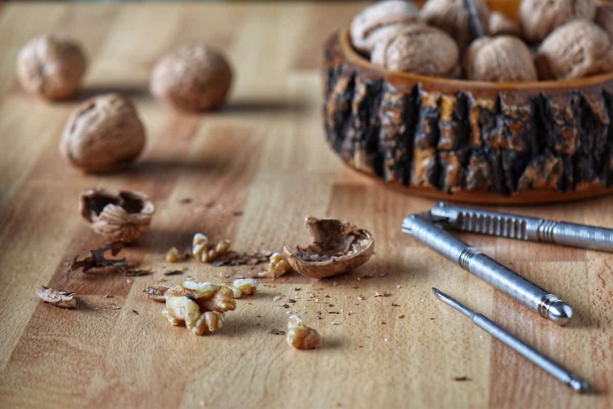 Whole and cracked open walnuts are pictured along with a nut cracker.