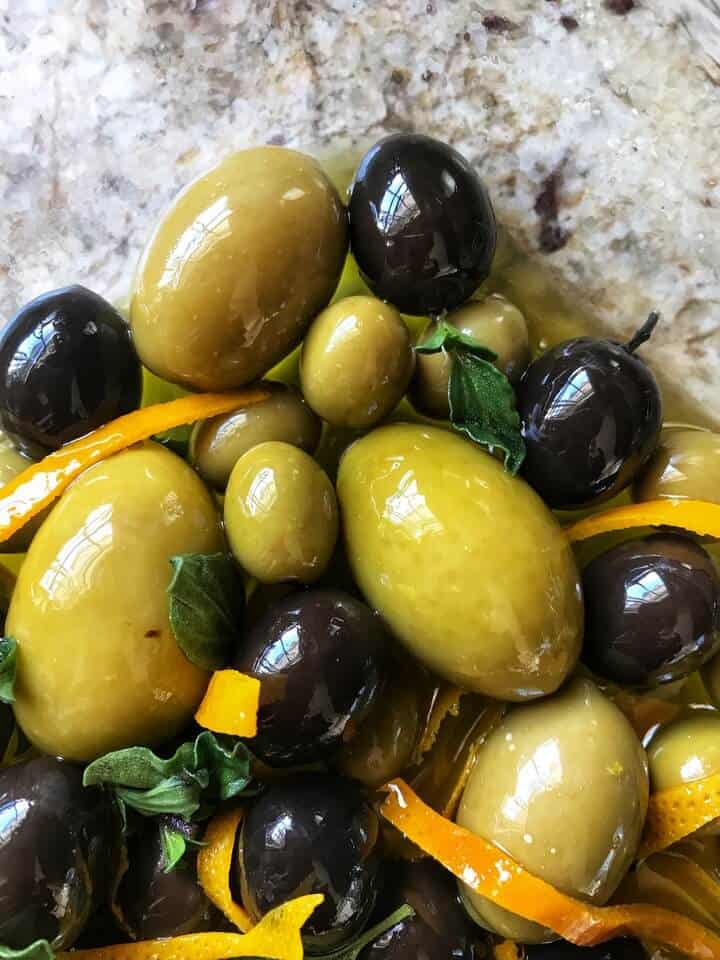 An overhead shot of marinated olives with orange zest and oregano.