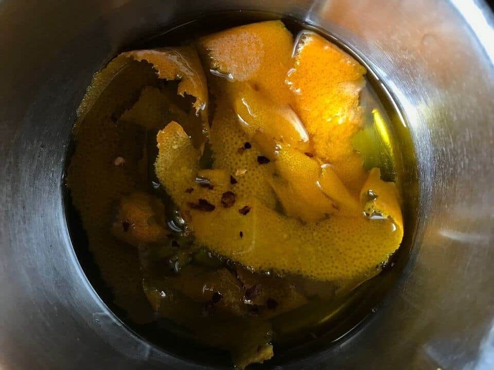 The infusion of the olive oil with orange zest in a small pot.