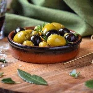 A close up shot of marinated olives in a brown terra cotta serving dish