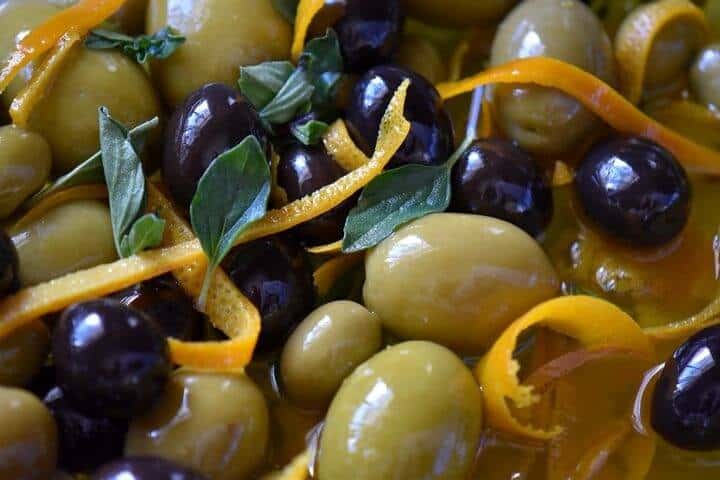 A close up shot of green and black marinated olives with oregano and slivers of orange zest.