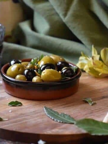 A round serving dish filled with black and green olives which have been marinated with olive oil and orange zest.