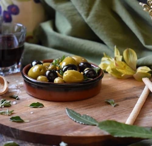 A round serving dish filled with black and green olives which have been marinated with olive oil and orange zest.