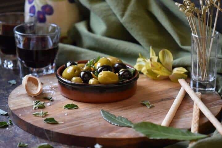 A round serving dish filled with black and green olives which have been marinated with olive oil and orange zest.