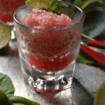 A glass of watermelon lime granita ice decorated with mint leaves and a piece of lime.