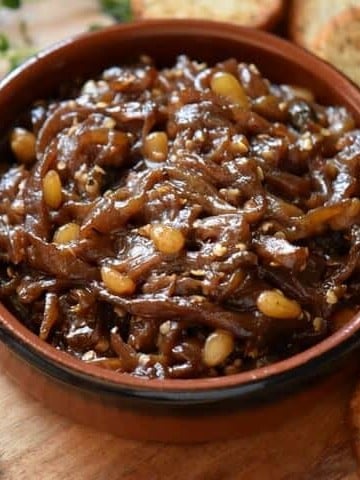 An overhead shot of roasted eggplant caponata in a round ceramic dish surrounded by crispy baguette slices.