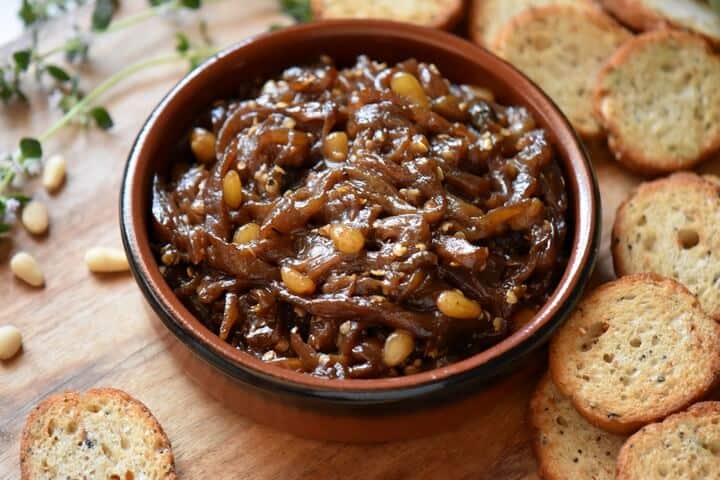 An overhead shot of roasted eggplant caponata in a round ceramic dish surrounded by crispy baguette slices.