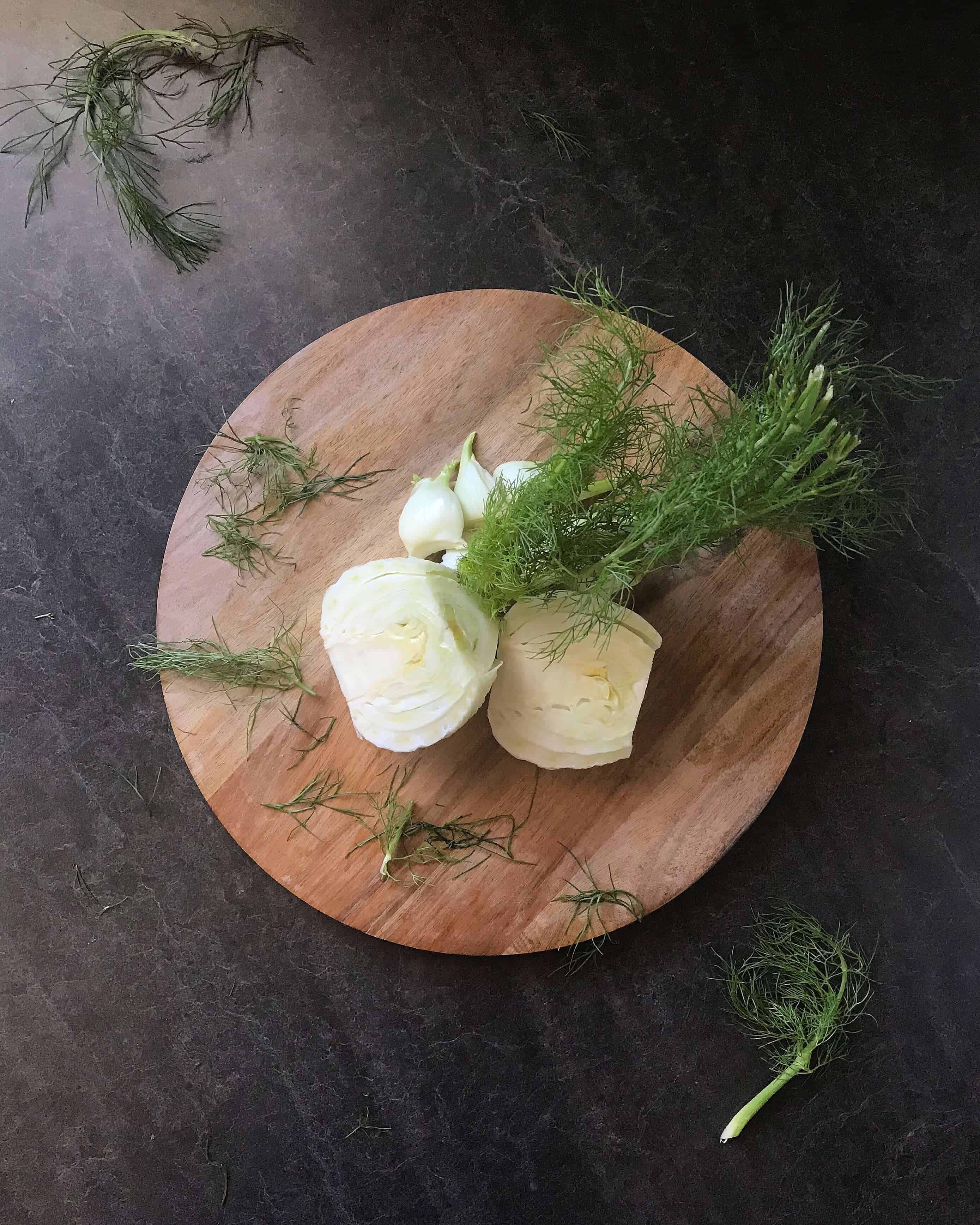 An overhead shot of fresh fennel bulbs, cut in half, placed on a wooden board.