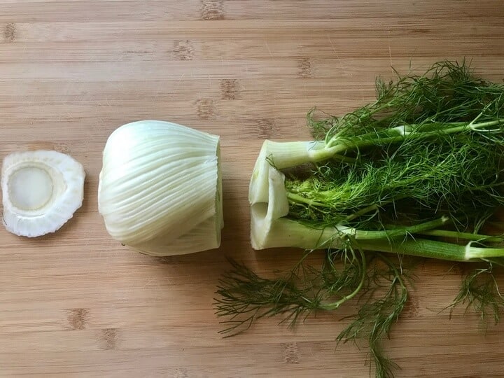 A fennel has been cut into three sections: the stalks and the fennel fronds, the bulb and the bottom root part. 